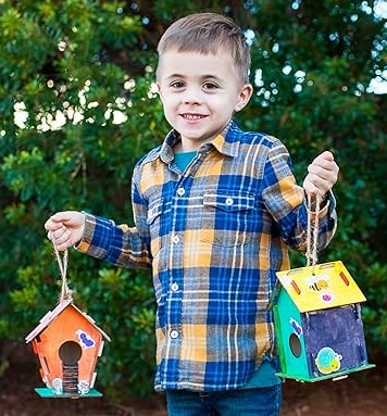 Boy holding two decorated wooden birdhouses.